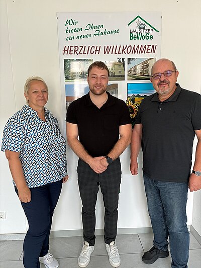 Der neue Auszubildende S. Zink (Mitte) mit C. Blödgen und S. Menzebach vor einem Willkommens-Plakat der Lausitzer BeWoGe.